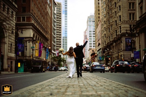Newly married couple stroll through Philadelphia streets near City Hall, hands raised high in triumph. Their radiant joy is evident in this celebratory scene.
