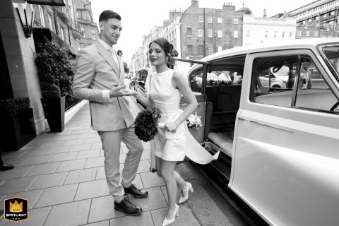 A couple exits a car on urban streets in the City of London, captured in a black-and-white shot. The candid moment shows them stepping into the bustling city.