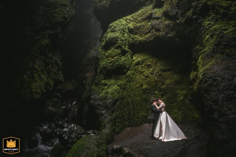On Iceland's Snaefellsnes Peninsula, a couple shares an embrace in a moss-covered canyon. The romantic portrait highlights their connection within the rugged, green landscape.