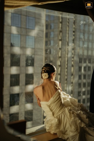 A bride is seated on a window sill in Sao Paulo. The urban city view stretches out behind her, creating a striking backdrop for her wedding day.