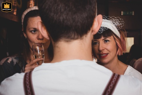 The bride and her guests share a candid moment at a pub reception in Birmingham, UK. The intimate photo captures a circle of shared words and glances, reflecting a warm and joyous atmosphere.