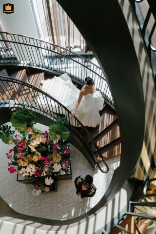 At Raffles Hotel Boston, a stunning top-down view captures the bride gracefully descending an elegant spiral staircase. Her wedding gown flows behind like a cascade, creating a timeless and artistic moment filled with anticipation and beauty.