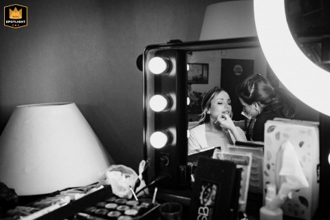 A bride has her makeup done at home in Feytiat, France. The black-and-white shot, captured in a mirror, shows a quiet and candid moment of preparation before the wedding ceremony.