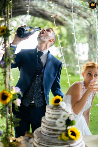 After cutting the cake at Tenuta Monticello, the groom drinks sparkling wine directly from the bottle. This celebratory act captures a moment of spontaneous fun and joy during the wedding reception.