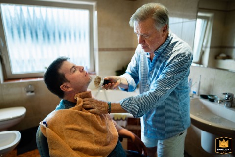 The groom gets a traditional shave from his father at Villa Toskana. This intimate moment of preparation shows a quiet rite of passage full of emotion before the wedding.
