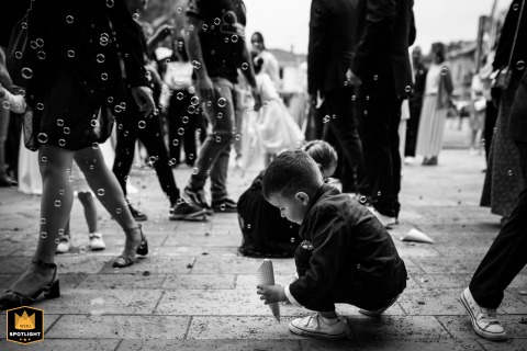 A black-and-white photo from Haute-Garonne captures a child squatting with a bubble cone. A group of people stands behind him, creating a candid and playful wedding moment.