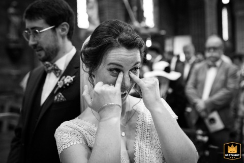 At église de Samatan in Gers, a woman gently wipes away tears of happiness in a touching black and white moment. The emotional scene captures pure joy and heartfelt emotion during a meaningful, unforgettable wedding celebration.