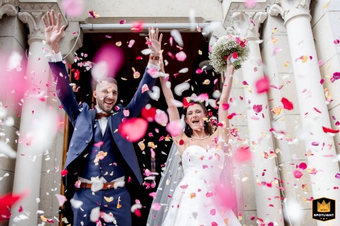 A low-angle shot captures a bride and groom exiting a church in Saint-Martin-d'Uriage, France. They are showered with petals, creating a beautiful and celebratory moment at the conclusion of their ceremony.