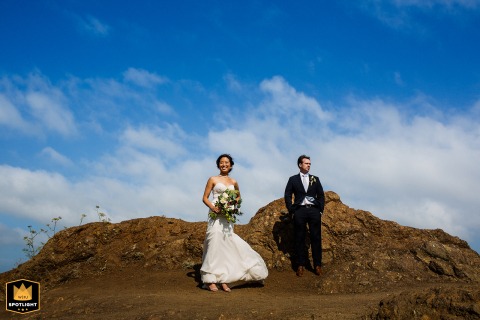 A newlywed couple stands close together beneath a clear blue sky at Battery Yates in Sausalito, California. Framed by rugged rock outcroppings, their quiet poses captures the serenity of their wedding day.