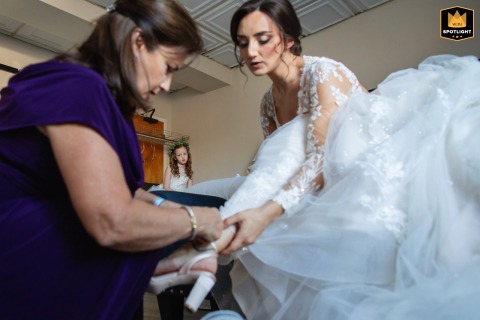 A flower girl watches from a distance as a bride's mother helps her put on her shoes at The Shore Club. The candid photograph highlights the loving, intimate moments before a wedding.