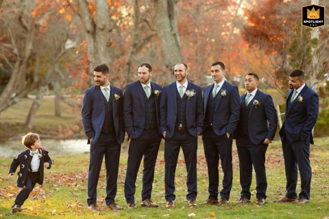 Groomsmen line up for a formal photograph at The Shore Club in Spring Lake, New Jersey. A young ring bearer, however, runs and plays around them, adding a touch of humor to the scene.