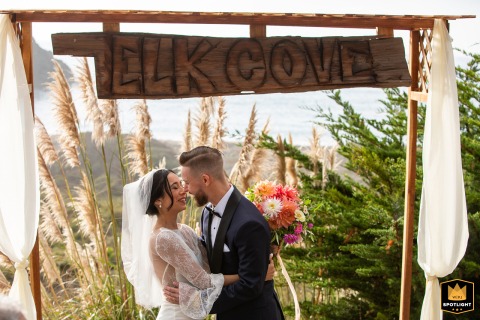 Under an altar at Elk Cove Inn, a bride and groom share their first kiss. The romantic image, marking the end of their ceremony, captures the couple's joy in Mendocino, California.