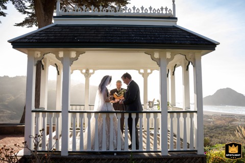 A bride and groom are captured during their wedding ceremony inside a charming gazebo at Elk Cove Inn. The intimate scene is framed by the wooden structure, creating a romantic scene.