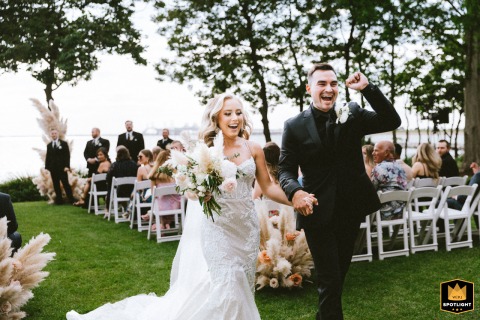 A bride and groom are captured at the Chesapeake Bay Golf Club, joyfully walking out at the end of their wedding ceremony. They are both smiling brightly as they celebrate becoming husband and wife.