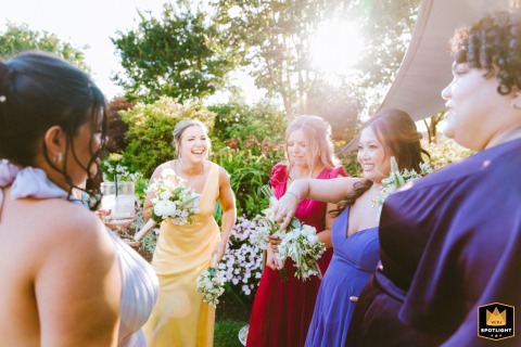 At The Inn at Herrington Harbour, the bride and her bridesmaids laugh and talk after the wedding ceremony. The sun shines from behind the trees, creating a warm and radiant scene.