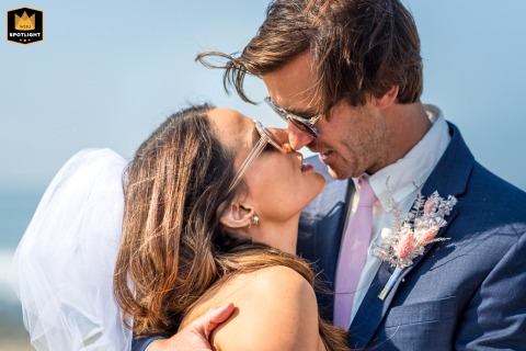 On a beach in Ventura, California, a newlywed couple shares a loving and passionate kiss. They are captured smiling at each other in the bright sunshine after their wedding ceremony.
