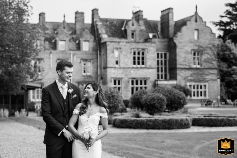 A black-and-white portrait of a couple at Shendish Manor. They are positioned off-center, with the grand venue visible in the background, creating a classic and timeless wedding photograph.