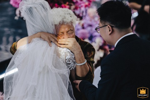 An elderly grandmother in Kaifeng, China, holds her granddaughter, the bride, and weeps with joy at a wedding.