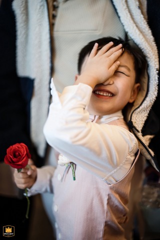 Little Boy Holding Rose Shyly Covers Eye as Newlyweds Kiss at Shanghai Wedding Cute boy covers eye as newlyweds kiss at Shanghai's Zitong Wedding Venue, holding a rose, shyly joyous.