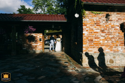 Capturing a Polish couple's entrance into their wedding reception, bathed in contrasting light Polish newlyweds enter their reception venue, captured in contrasting light, from a distance, surrounded by guests.