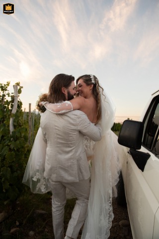 Uco Valley Kiss: A Romantic Wedding Photojournalist Moment in White and Love A wedding photojournalist captures a romantic kiss between the bride and groom after their ceremony in Valle de Uco, Mendoza, Argentina. Both are wearing white and standing by a white car.