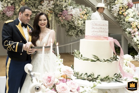 Slicing Cake with a Sword at the Mandarin Oriental, a Photojournalist's Unique Perspective A wedding photojournalist captures a couple cutting their cake with a sword at the Mandarin Oriental in Bangkok. A man behind looks like a cake topper.