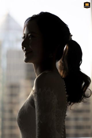 Plaza Athenee Bride's Quiet Gaze Amidst a Bangkok High-rise Skyscraper Vista A wedding photojournalist captures a portrait of a bride by a window in a high-rise unit, with skyscrapers visible in the background at the Plaza Athenee in Bangkok.