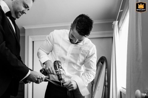 Pre-Ceremony Preparation: Groomsmen Help the Groom with His Belt in Melbourne A documentary-style photograph captures a candid moment at a groom's home in Melbourne, Australia. The image shows the groomsmen helping the groom with his belt as they prepare for the wedding.