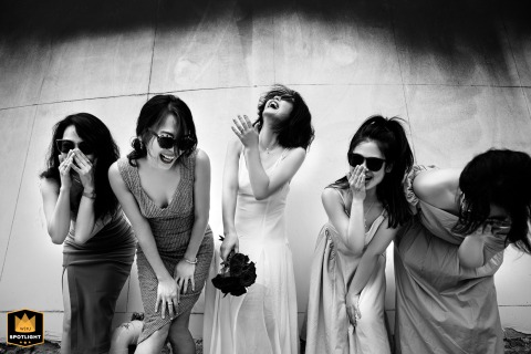 A documentary photograph captures a candid and joyful scene at a hotel in Fujian, China. The image shows a bride laughing alongside her bridesmaids during the wedding day celebration.