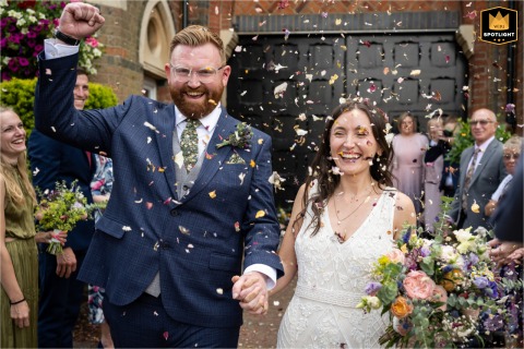 Celebratory Fist Pump for a St Albans Groom in Confetti A documentary-style photograph captures a bride and groom at the St Albans Register Office in Hertfordshire, England. The image shows the groom walking through confetti while he fist pumps the air in celebration.