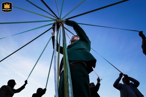Château Flojague's Groomsmen Embrace Joyful French Wedding Traditions A documentary-style photograph captures the groom and his groomsmen playing a traditional ribbon game at Château Flojague in Saint-Genès-de-Castillon, France. The image portrays a joyful moment during the wedding celebration.