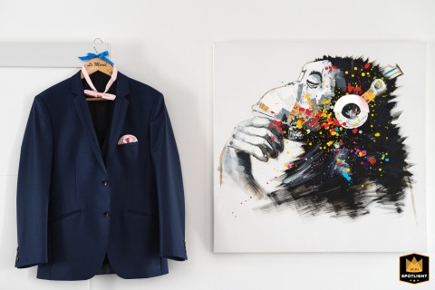 Groom's jacket and bow tie with a bewildered monkey painting In Haute-Garonne, a wedding photographer captures a groom's attire at his home during preparations. The detail shot features his wedding jacket and bow tie hung before a painting of a perplexed monkey listening to music.