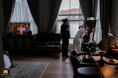 Unveiling Beauty, A Bride's Stillness, Pistol-Poised Freeze Frame in View At Six Senses Kocataş Mansions, İstanbul, a WPJA photographer captures a unique preparation moment. The bride checks her makeup as a television in the background shows a pistol and freeze frames.
