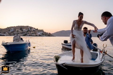 Symi Sunset: A Bride's Grand Arrival by Boat On the island of Symi, Greece, a wedding photographer captures a beautiful sunset arrival. The image shows a couple arriving by boat at the restaurant dock as a videographer assists the bride.