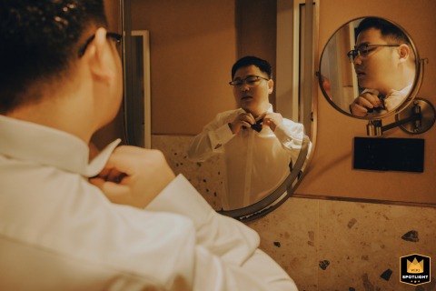 Groom Adjusting Traditional Chinese Wedding Attire In The Morning Light Groom in Kaifeng, China, adjusts his traditional Chinese wedding attire in the morning, looking in a mirror.