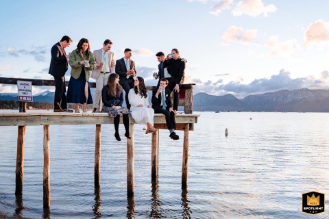Relaxing Over Water: Lake Tahoe Newlyweds and Friends Enjoy a Sunset Lake Tahoe, California: Newlyweds and friends relax on a hanging bridge, enjoying drinks at sunset after the wedding.