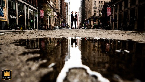 City Love Reflected: Philadelphia Couple's Hands, United in Urban Puddle Couple holding hands on a Philadelphia street, their reflection visible in a puddle amidst the cityscape.