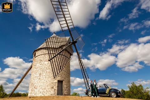 Montcuq's Kiss: A Timeless Love, A French Windmill, A Classic Car Bridal couple kisses in front of a windmill and classic car in Montcuq, France.