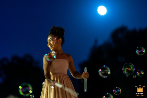 Moonlit Bubbles: Painted Girl Entertains Children At Whimsical Wedding Reception Outdoors Young girl with face paint blows bubbles for kids at a wedding reception under the moonlight.