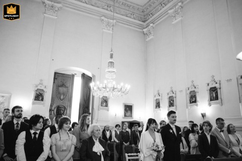 Newly Married Couple Stands Together at Altar of Beautiful Poland Church, Guests Watching Poland is the location where a newly married couple stands together at the altar of a beautiful church with their gathered wedding guests looking on.