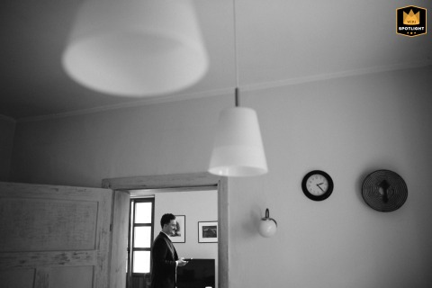 Groom Waits Patiently in Sunlit Polish Home While Bride Finishes Makeup Touches In a home in Poland, the groom waits patiently and silently in a sunlit room for his bride to finish her final touches of make-up before the ceremony begins.