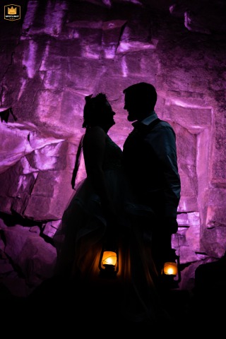 Newlyweds Hold Lanterns Exploring Dark Cave Illuminated By A Spooky Purple Glow Inside The Grotto, Aspen, Colorado, the newlyweds hold lanterns while exploring the dark cave, illuminated by an off-camera flash that casts a spooky purple glow on the scene.