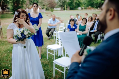 Budapest, Hungary, is the location where a tearful bride wipes her eyes while listening intently to her groom's heartfelt vows, surrounded by close family and friends.