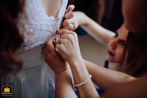 Inside a hotel in Hungary, delicate hands work with quiet focus, diligently fastening the final buttons of the intricate wedding dress right before the bride's big moment.