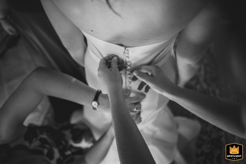 Intimate Moment: Fastening Delicate Buttons at Castello di Modanella During the wedding preparations at the Castello di Modanella, Tuscany, the intimate "getting ready" moment focuses tightly on hands clasping the delicate buttons at the back of the bride's dress.