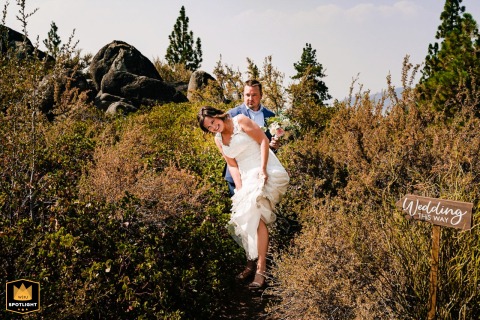 Playful Kiss Behind Bushes Next to 'Wedding This Way' Sign In South Lake Tahoe, CA, immediately following the wedding, the playful couple shares a moment of affection, sneaking behind the bushes next to a sign reading, 'Wedding This Way.'