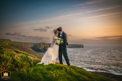 Bride and groom embracing at sunset in Kilkee, Ireland, with a romantic and dramatic sky in the background.