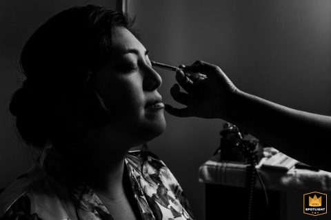 Black and white close-up in Playa del Carmen showing the final touches of makeup, with the makeup artist’s hand reaching into the frame.