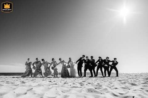 Bridal party gathered in a harmonious formation at Bank Street Beach in Harwich, MA, illuminated by natural light and surrounded by the ocean and sand, highlighting their joyful bonds and shared celebration.