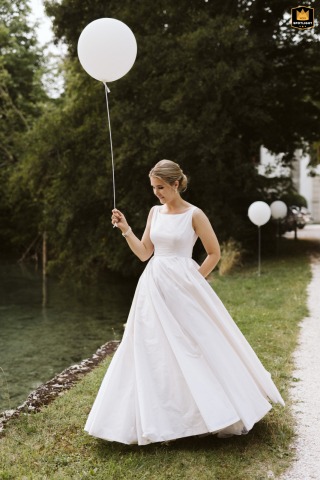 At Austria's Schloss Kammer reception venue, the bride elegantly strolls across the grounds, holding a single celebratory balloon.
